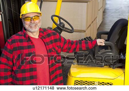 Man standing by fork lift truck smiling View Large Photo Image Stock Photo - Man standing by fork lift truck smiling. Fotosearch