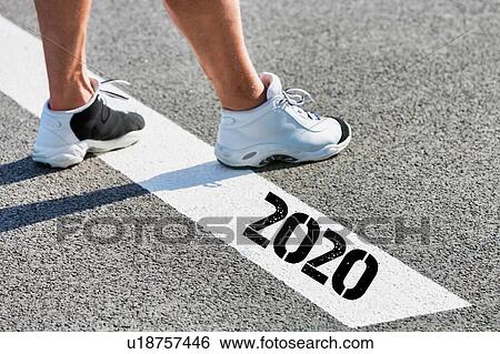 Stock Photograph - Man standing on stepping on white line with year 2020 sign. Fotosearch