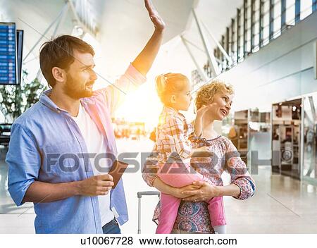 Stock Photo - Man waving and holding his passport boarding pass while his wife is carrying their daughter. Fotosearch