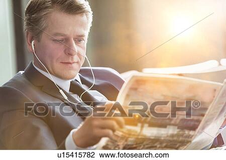 Mature attractive businessman reading newspaper while waiting and listening to music in airport View Large Photo Image Stock Image - Mature attractive businessman reading newspaper while waiting and listening to music in airport. Fotosearch