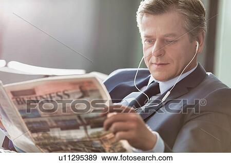 Stock Photo - Mature attractive businessman reading newspaper while waiting and listening to music in airport. Fotosearch