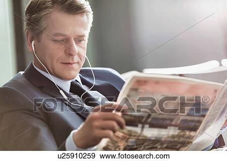 Stock Photo - Mature attractive businessman reading newspaper while waiting and listening to music in airport. Fotosearch
