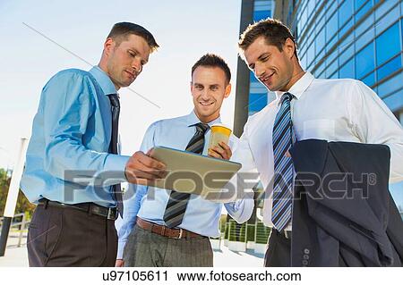 Mature attractive businessman showing and discussing plans over digital tablet with colleagues against office building View Large Photo Image Stock Image - Mature attractive businessman showing and discussing plans over digital tablet with colleagues against office building. Fotosearch
