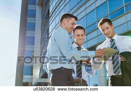 Stock Photo - Mature attractive businessman showing and discussing plans over digital tablet with colleagues against office building. Fotosearch