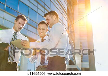 Mature attractive businessman showing and discussing plans over digital tablet with colleagues against office building View Large Photo Image Stock Photograph - Mature attractive businessman showing and discussing plans over digital tablet with colleagues against office building. Fotosearch