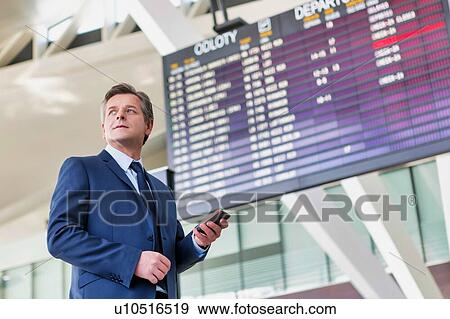 Mature attractive businessman using smartphone while standing against flight display screen in airport View Large Photo Image Stock Photo - Mature attractive businessman using smartphone while standing against flight display screen in airport. Fotosearch