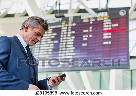 Mature attractive businessman using smartphone while standing against flight display screen in airport View Large Photo Image Stock Photo - Mature attractive businessman using smartphone while standing against flight display screen in airport. Fotosearch