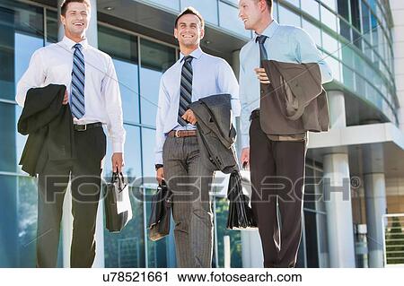 Stock Image - Mature attractive businessmen walking while talking against office building after work. Fotosearch