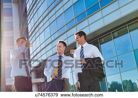 Stock Photo - Mature attractive businessmen walking while talking against office building after work. Fotosearch