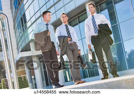 Stock Photography - Mature attractive businessmen walking while talking against office building after work. Fotosearch