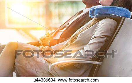 Picture - Mature businessman and young attractive businesswoman sleeping while waiting for boarding in their gate at airport. Fotosearch