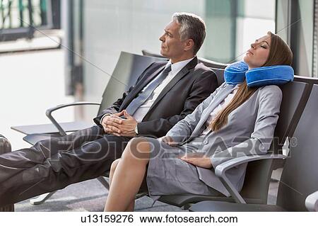 Stock Photograph - Mature businessman and young attractive businesswoman sleeping while waiting for boarding in their gate at airport. Fotosearch