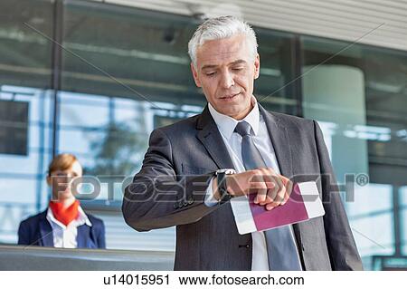Stock Image - Mature businessman checking time on his watch after checked in at airport. Fotosearch