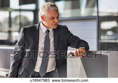 Mature businessman checking time on his wristwatch in airport View Large Photo Image Stock Image - Mature businessman checking time on his wristwatch in airport. Fotosearch