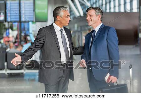 Stock Photograph - Mature businessman gesturing while talking to business partner in airport . Fotosearch