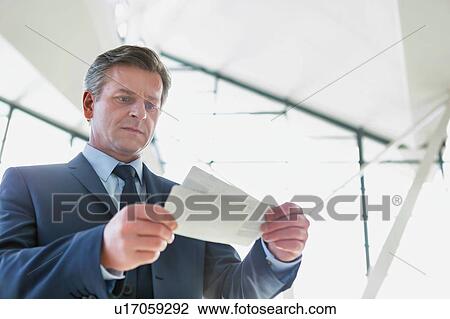 Stock Image - Mature businessman looking at his boarding pass in airport. Fotosearch