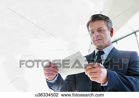 Mature businessman looking at his boarding pass in airport View Large Photo Image Stock Image - Mature businessman looking at his boarding pass in airport. Fotosearch