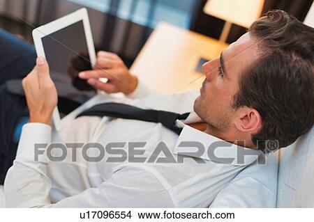 Mature businessman lying on bed while using digital tablet at home View Large Photo Image Picture - Mature businessman lying on bed while using digital tablet at home. Fotosearch