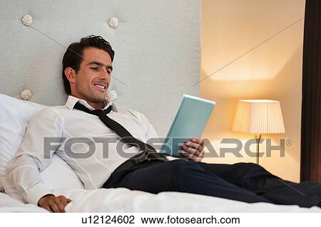 Stock Image - Mature businessman lying on bed while using digital tablet at home. Fotosearch