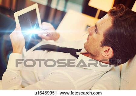 Stock Image - Mature businessman lying on bed while using digital tablet at home. Fotosearch