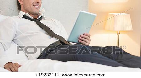 Mature businessman lying on bed while using digital tablet at home View Large Photo Image Stock Image - Mature businessman lying on bed while using digital tablet at home. Fotosearch