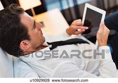 Stock Photo - Mature businessman lying on bed while using digital tablet at home. Fotosearch