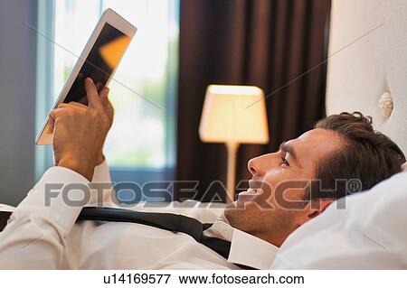 Stock Photo - Mature businessman lying on bed while using digital tablet at home. Fotosearch