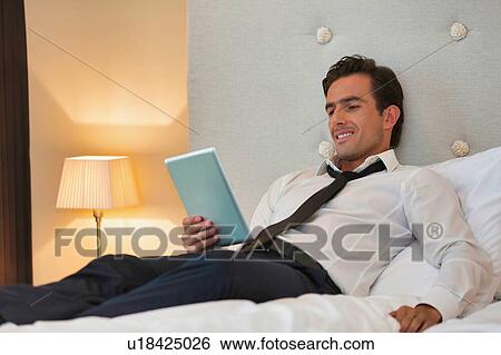 Mature businessman lying on bed while using digital tablet at home View Large Photo Image Stock Photograph - Mature businessman lying on bed while using digital tablet at home. Fotosearch