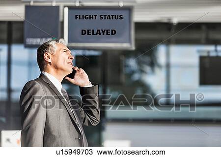 Stock Image - Mature businessman making report on his delayed flight while standing at his boarding gate in airport. Fotosearch