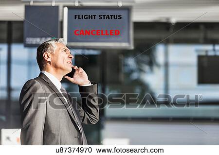 Stock Image - Mature businessman making report on his cancelled flight while standing at his boarding gate in airport. Fotosearch