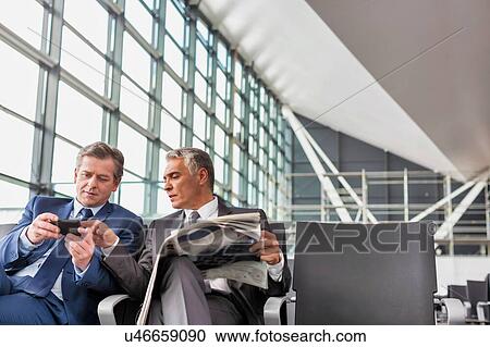 Stock Image - Mature businessman playing games on his phone while sitting and waiting for boarding in airport. Fotosearch