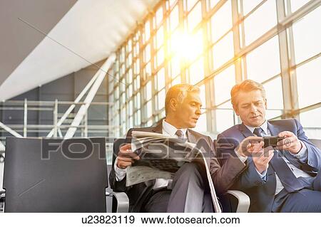 Stock Photo - Mature businessman playing games on his phone while sitting and waiting for boarding in airport. Fotosearch