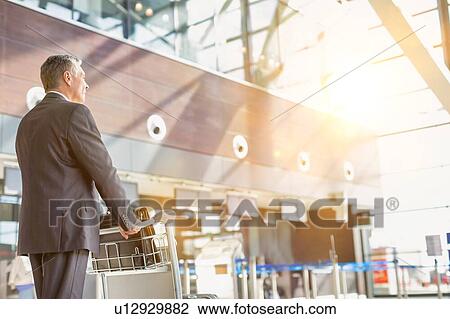 Stock Image - Mature businessman pushing baggage cart for check in at airport. Fotosearch
