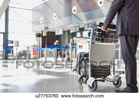 Stock Image - Mature businessman pushing baggage cart for check in at airport. Fotosearch