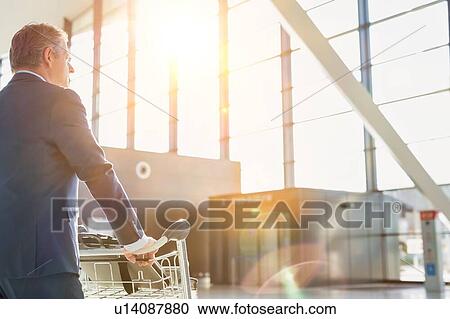 Stock Image - Mature businessman pushing luggage cart for check in at airport . Fotosearch