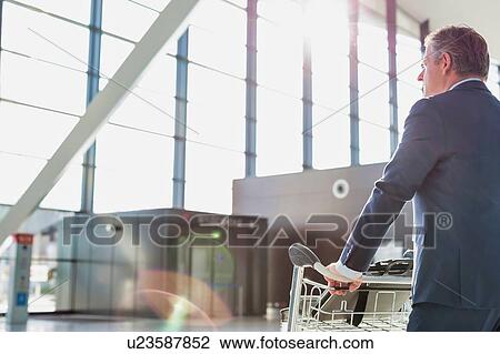 Mature businessman pushing luggage cart for check in at airport View Large Photo Image Stock Image - Mature businessman pushing luggage cart for check in at airport . Fotosearch