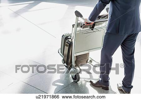 Stock Photograph - Mature businessman pushing luggage cart for check in at airport . Fotosearch