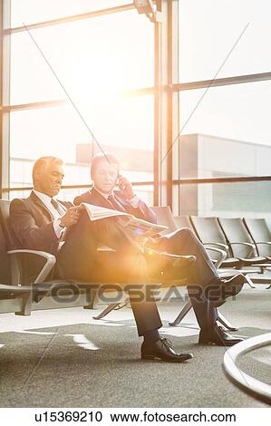 Mature businessman reading news paper while the other businessman is talking on smartphone in airport View Large Photo Image Stock Image - Mature businessman reading news paper while the other businessman is talking on smartphone in airport. Fotosearch