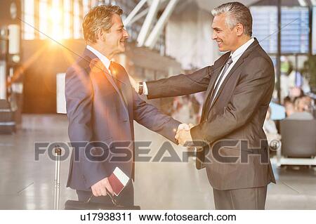 Mature businessman shaking hands with business partner in airport View Large Photo Image Stock Image - Mature businessman shaking hands with business partner in airport. Fotosearch