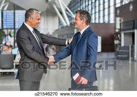 Stock Image - Mature businessman shaking hands with business partner in airport. Fotosearch