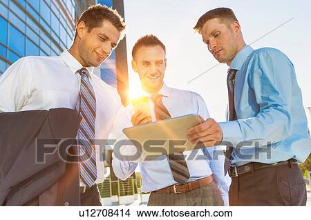 Picture - Mature businessman showing business plan on digital tablet with his colleagues. Fotosearch