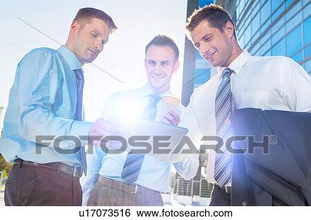Stock Photograph - Mature businessman showing business plan on digital tablet with his colleagues. Fotosearch