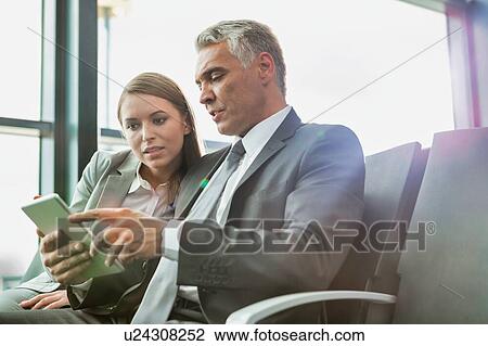 Stock Image - Mature businessman showing digital tablet to young attractive businesswoman in airport. Fotosearch