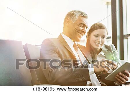 Stock Photography - Mature businessman showing digital tablet to young attractive businesswoman in airport. Fotosearch