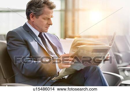 Picture - Mature businessman sitting and reading newspaper while waiting for boarding in airport. Fotosearch
