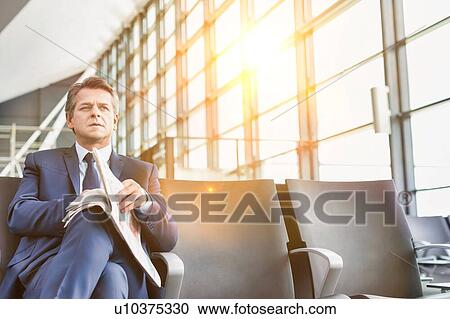 Mature businessman sitting and reading newspaper while waiting for boarding in airport View Large Photo Image Stock Image - Mature businessman sitting and reading newspaper while waiting for boarding in airport. Fotosearch