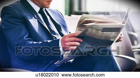 Stock Image - Mature businessman sitting and reading newspaper while waiting for boarding in airport. Fotosearch