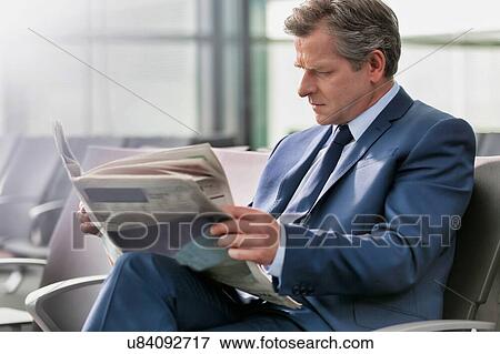 Stock Photo - Mature businessman sitting and reading newspaper while waiting for boarding in airport. Fotosearch