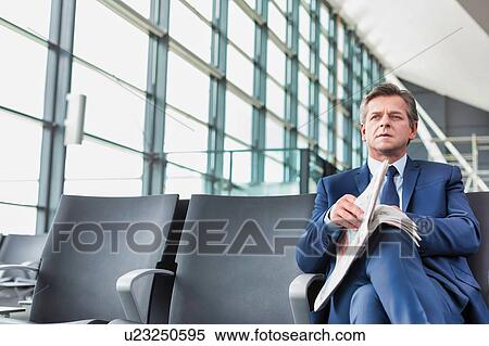 Stock Photography - Mature businessman sitting and reading newspaper while waiting for boarding in airport. Fotosearch