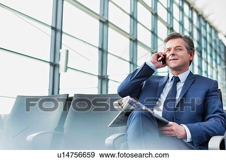 Mature businessman sitting and talking on smartphone while waiting for boarding in airport View Large Photo Image Stock Photo - Mature businessman sitting and talking on smartphone while waiting for boarding in airport. Fotosearch
